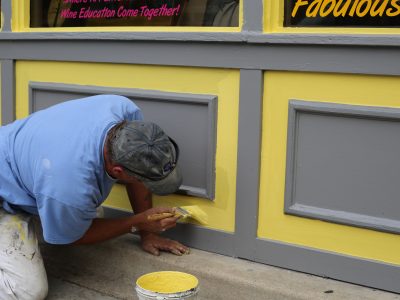 Un homme peint la devanture d'un magasin.